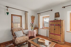 Un salón acogedor con un sillón estampado, un mueble de madera y una mesa de centro con superficie de vidrio.
