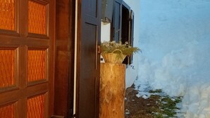 Eine Holztür mit Herzverzierung, ein Korb auf einem Holzpfosten und verschneiter Boden.