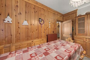 A wooden-paneled room with a bed, dresser, and a door leading to another room.
