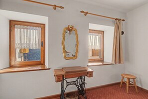 A room with a wooden desk, a sewing machine, a mirror, and a window with curtains.