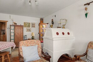 Una habitación tradicional con un aparador de madera, una cama con colcha estampada, un sillón con cojín y una estantería decorativa con varios objetos.