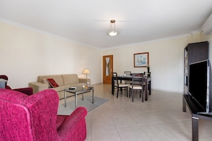 A living room with a sofa, a coffee table, a TV, and a dining area with chairs and a table.