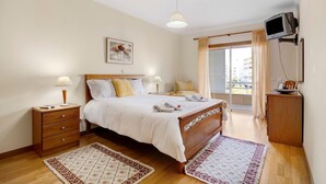 Une chambre à coucher avec un lit, des tables de chevet, une télévision et un balcon avec vue.