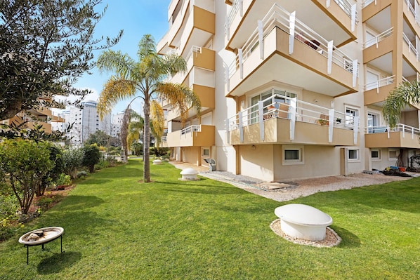 A multi-story hotel with balconies, a well-maintained lawn, and surrounding greenery.
