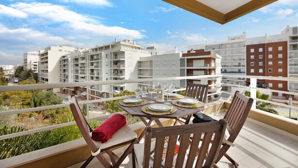 Un balcon avec une table dressée pour le repas, des chaises et une serviette rouge.