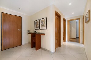 A hallway with a wooden door, a desk with a candle, and framed pictures on the wall.