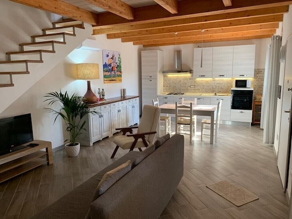 A modern interior with a staircase, a sofa, a dining area, and a kitchen with white cabinets and a brick backsplash.