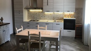 Een moderne keuken met witte kasten, een gasfornuis en een eethoek met een tafel en stoelen.
