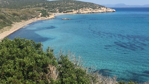 Een kustlandschap met helderblauw water, een zandstrand en groene heuvels.