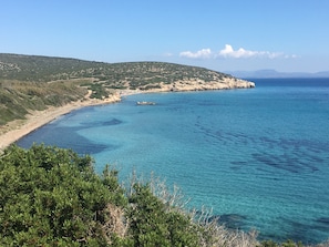 A coastal landscape with clear blue waters, sandy beach, and green hills.