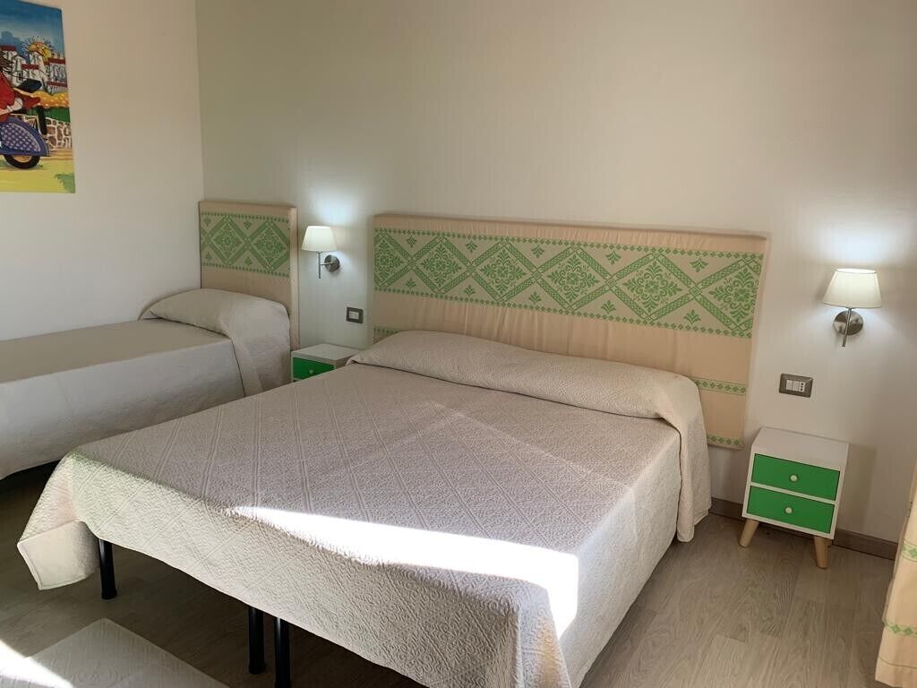 A hotel room with two beds, a green and beige headboard, bedside lamps, and a small green nightstand.