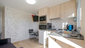 Une cuisine compacte équipée d’un four à micro-ondes, d’un four traditionnel et d’un évier, avec des placards en bois et un petit coin repas comprenant une table et des chaises.