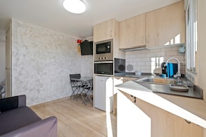 A compact kitchen with a microwave, oven, and sink, wooden cabinets, and a small dining area with a table and chairs.