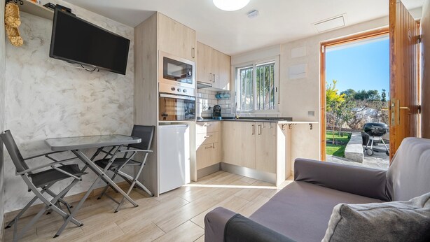 Un espace de vie compact comprenant un coin cuisine, un espace repas avec des chaises pliantes, un canapé et un téléviseur fixé au mur.