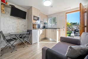 Un espace de vie compact comprenant un coin cuisine, un espace repas avec des chaises pliantes, un canapé et un téléviseur fixé au mur.