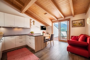 Eine moderne Küche mit Holzbalken, einem Essbereich mit einem roten Sofa und einem großen Fenster mit Blick auf die Berge.