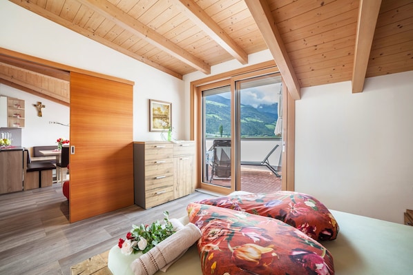 Ein Schlafzimmer mit Holzboden, einem Bett mit Blumenmuster-Bettwäsche, einer Schiebetür zu einem Balkon und Blick auf Berge.