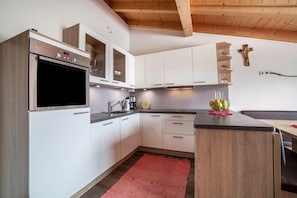 Eine moderne Küche mit weißen Schränken, einem Edelstahlbackofen und einer Holzbalkendecke.