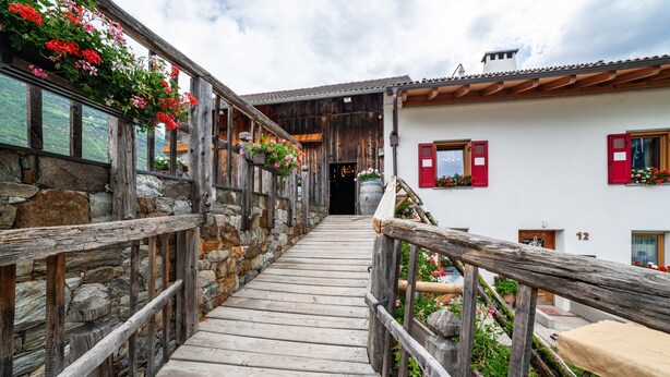 A wooden staircase leading to a building with stone walls and red shutters. - Apartment "Sagschneiderhof Golden Delicious" with Mountain View, Whirlpool & Wi-Fi (Plaus)