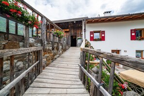 Una escalera de madera que lleva a un edificio con paredes de piedra y contraventanas rojas.