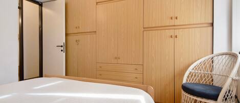 A bedroom with a bed, a wooden wardrobe, and a wicker chair.