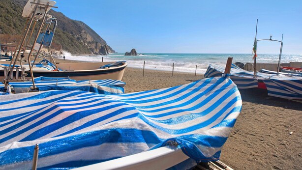 A beach with boats and a rocky cliff in the background.