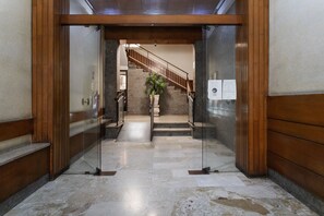 Un hall au sol en marbre, doté d’une entrée à ossature en bois, d’un escalier et d’une plante en pot.