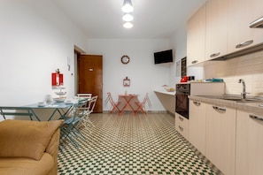 Une cuisine de taille réduite avec un carrelage à motifs, une table à manger avec des chaises, un canapé et un téléviseur fixé au mur.
