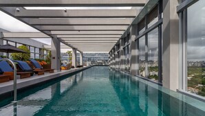 A long indoor swimming pool with a clear view of the cityscape through large windows.