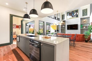 Uma cozinha moderna com ilha central, iluminação pendente e área de refeições com sofá e cadeiras.