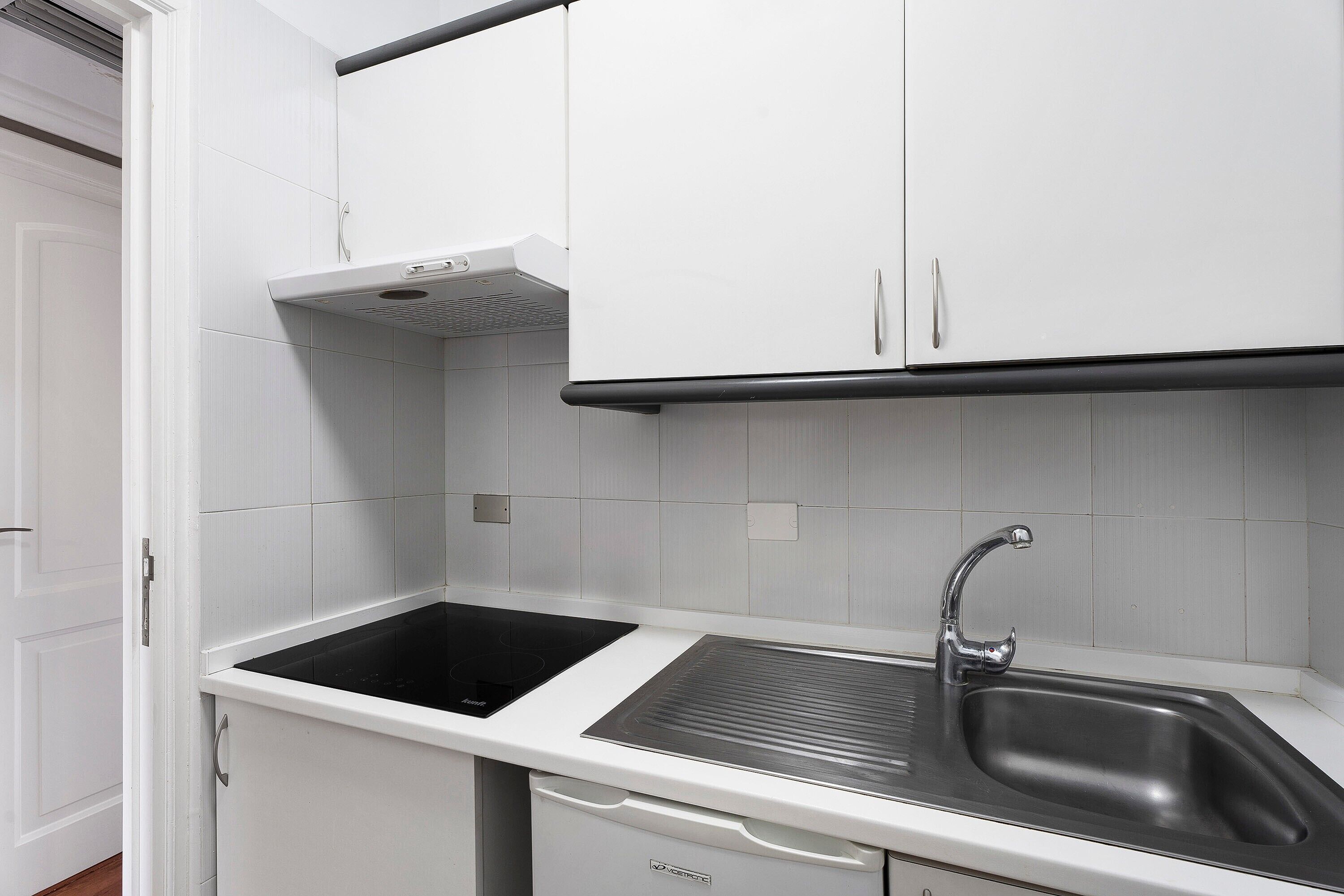 Cocina con armarios blancos, encimera negra, pileta de acero inoxidable y horno empotrado.