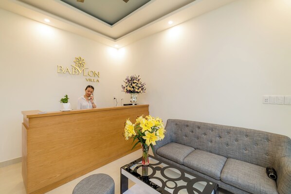 A reception area with a wooden desk, a receptionist, a grey sofa, and a vase of yellow flowers.