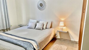 Un letto rifatto con copriletto bianco e grigio, diversi cuscini, una lampada da comodino e uno specchio montato a parete.