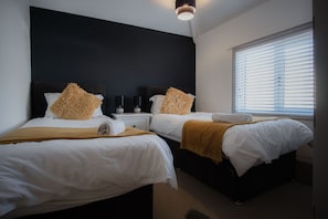 Two single beds with white linens and brown throw pillows, accompanied by matching nightstands and lamps.