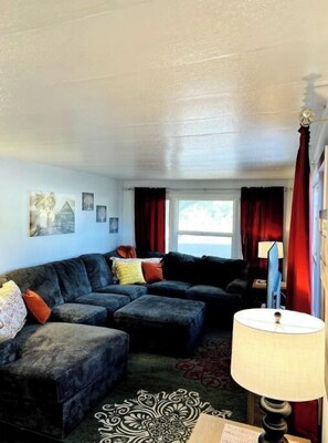 Relax in a cozy space with a sofa, ottoman, and area rug, surrounded by artwork and natural light.