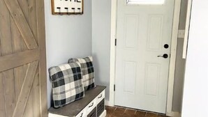 A hallway with a wooden bench, a 'HOME' sign, a white door, and a tiled floor.