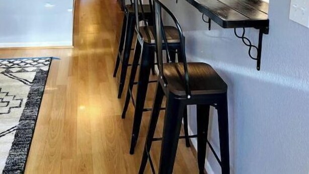 A modern kitchen with a bar area, wooden bar stools, and pendant lighting.