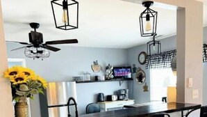 A modern kitchen with a bar area, featuring a wooden bar counter, black metal chairs, and pendant lighting.