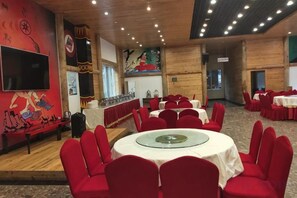 A banquet hall with round tables and red chairs, a large flat-screen TV, and a mural on the wall. - Heizhugou Midou Hotel (Ebian)