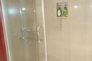 A glass-enclosed shower with a chrome handle and a towel rack. There are two bottles of liquid soap on a shelf above the shower. - Heizhugou Midou Hotel (Ebian)