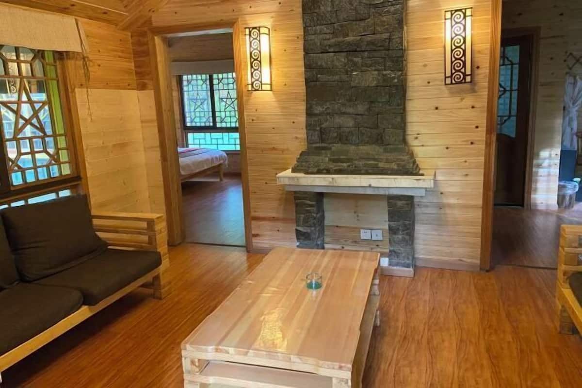 A cozy room with a wooden floor, a sofa, a table, a stone fireplace, and a bed in the background.