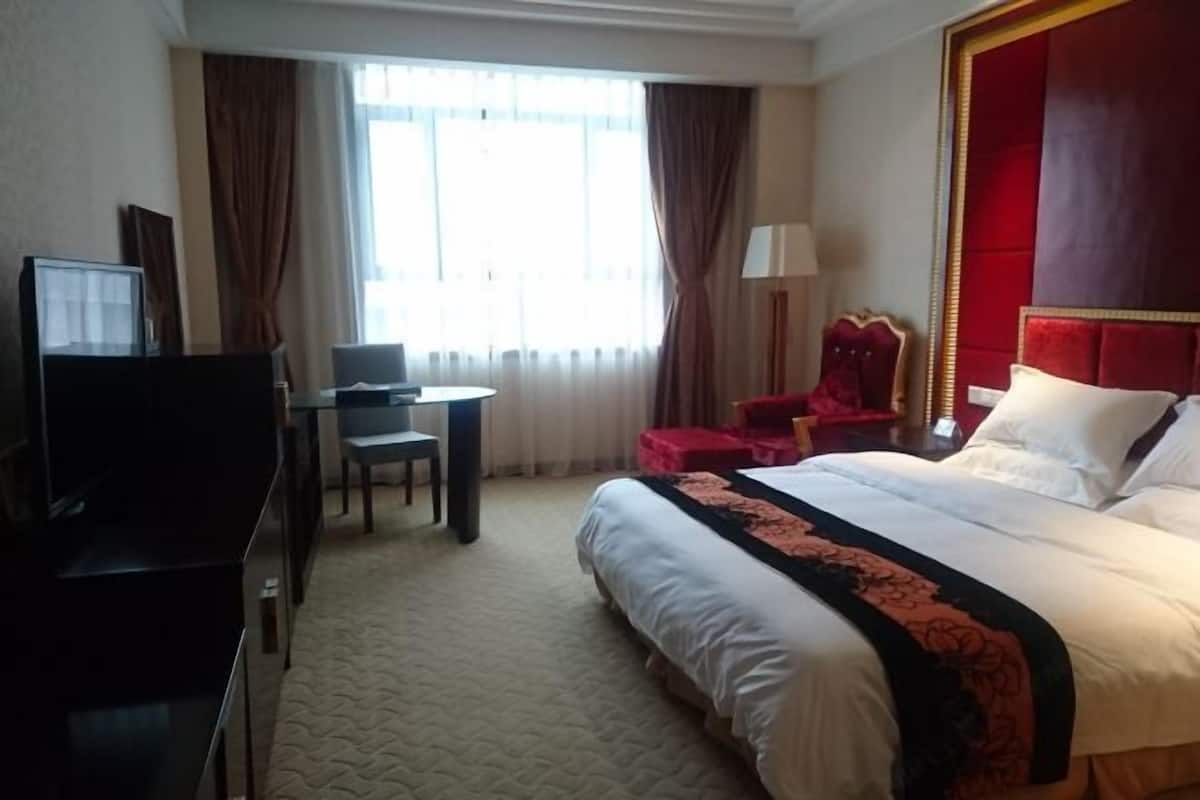 A hotel room with a bed, a desk, a chair, a TV, and curtains.