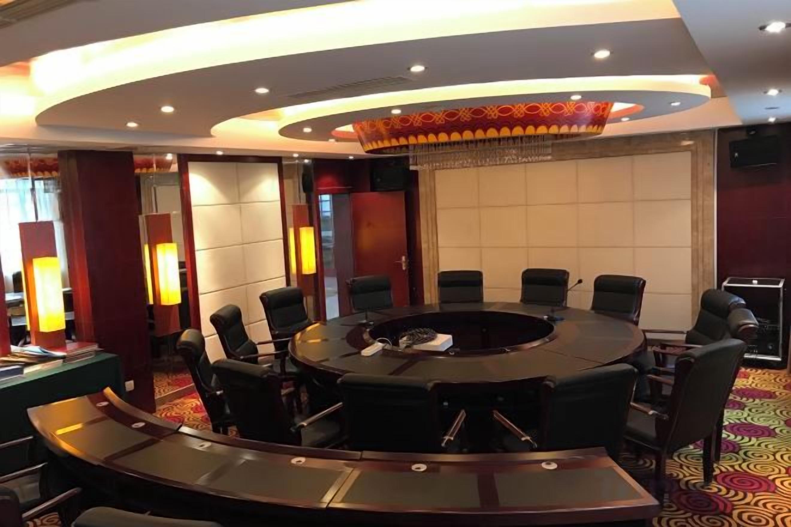 Un salón de conferencias con una mesa redonda, sillas y una pantalla grande.