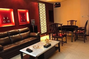 A modern living room with a leather sofa, a coffee table, and wooden chairs. - Heizhugou Midou Hotel (Ebian)