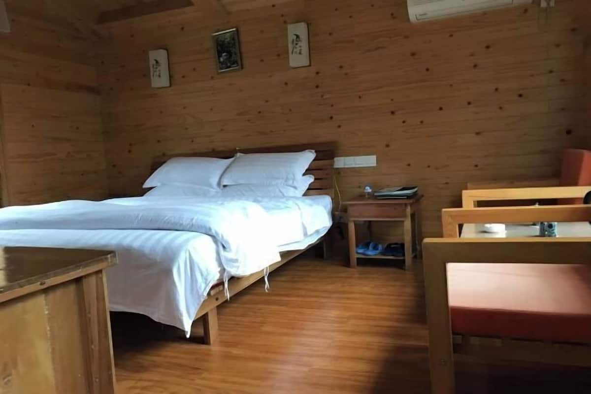 A wooden room with a bed, a nightstand, a chair, and a table.