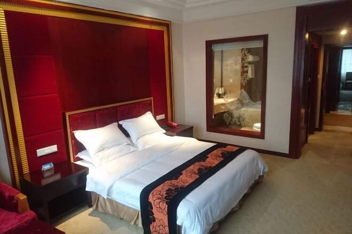 A hotel room with a large bed, a nightstand, a red upholstered headboard, a mirror, and a red chair.