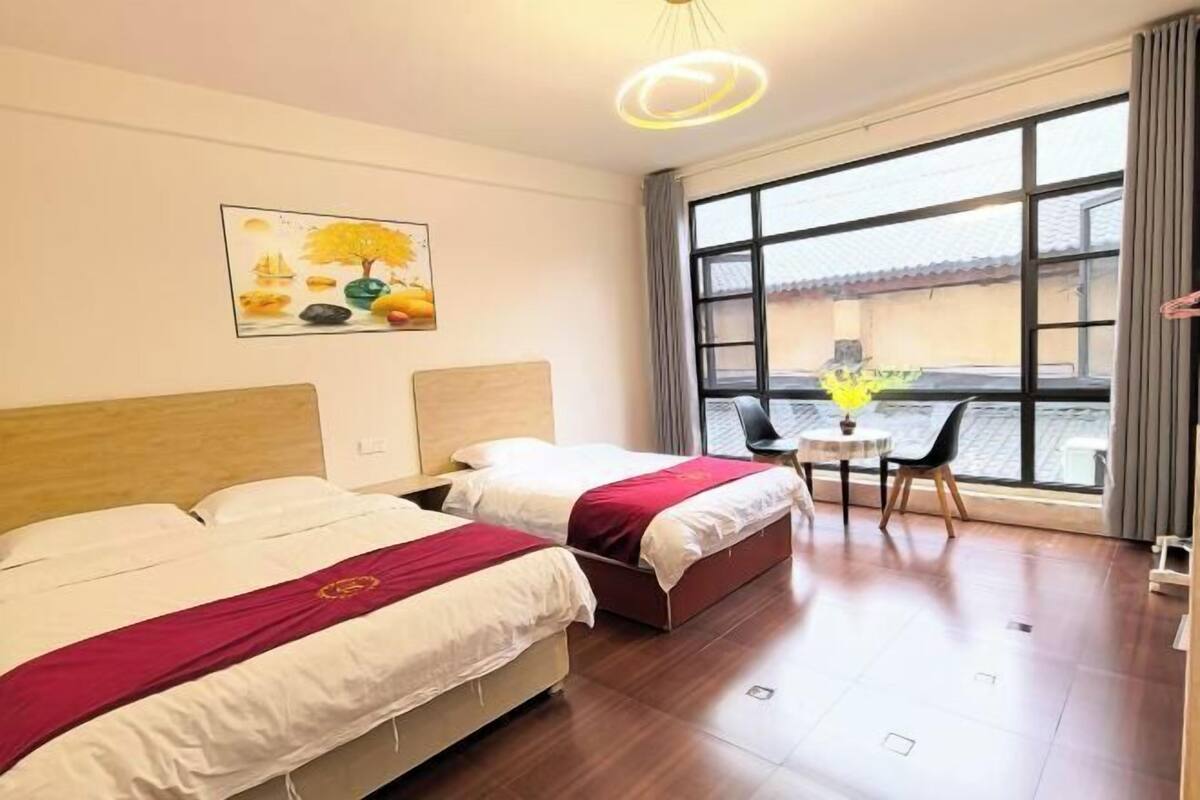 Une chambre d’hôtel avec deux lits, un tableau, une table avec des chaises et une grande fenêtre.