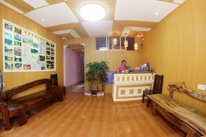 Zona de recepción con suelo de madera, mostrador de recepción y recepcionista. Hay bancos de madera y una planta en maceta.
