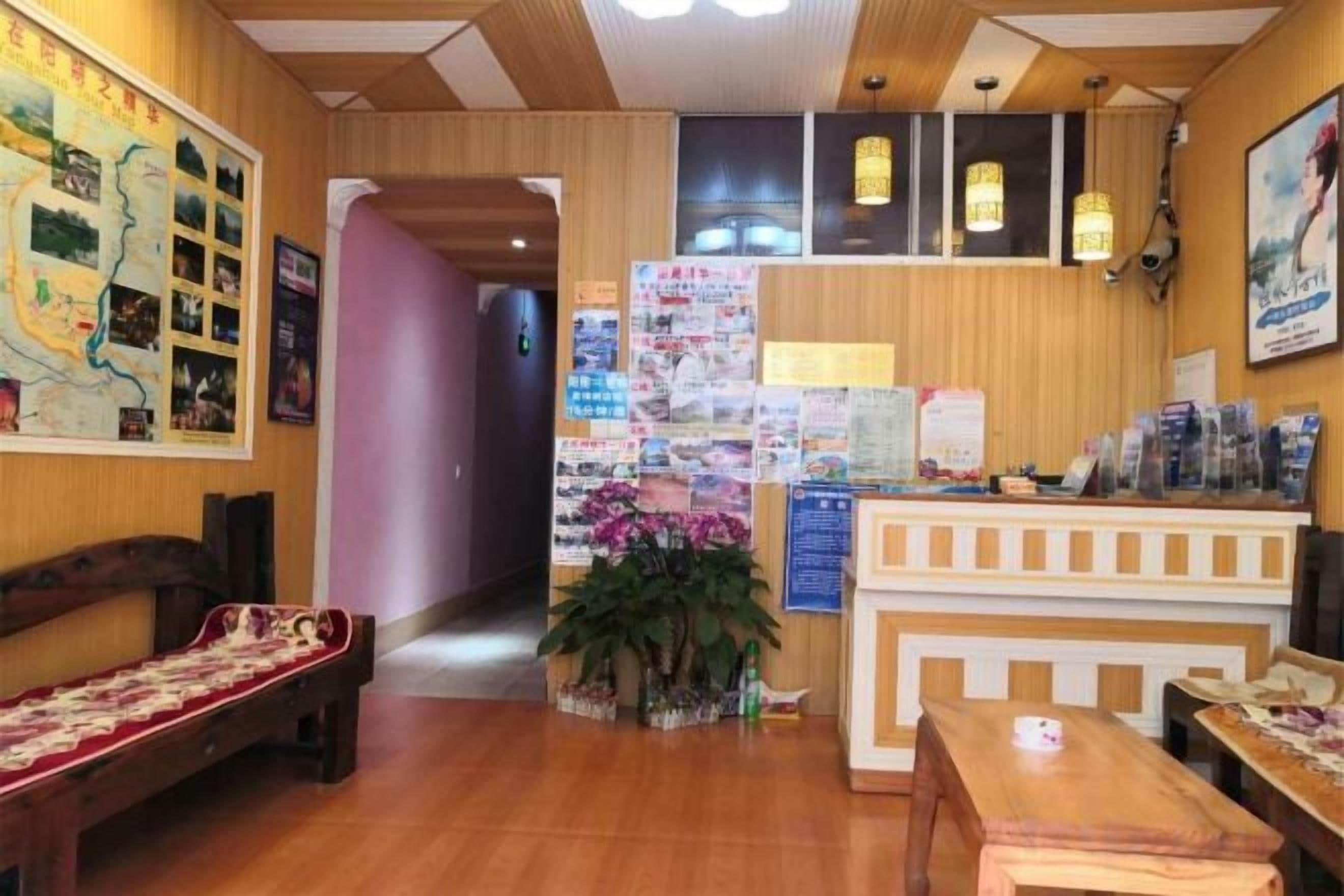 A hotel lobby with a reception desk, seating area, and a wall with informational posters.