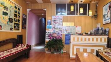 A hotel lobby with a reception desk, seating area, and a wall with informational posters.